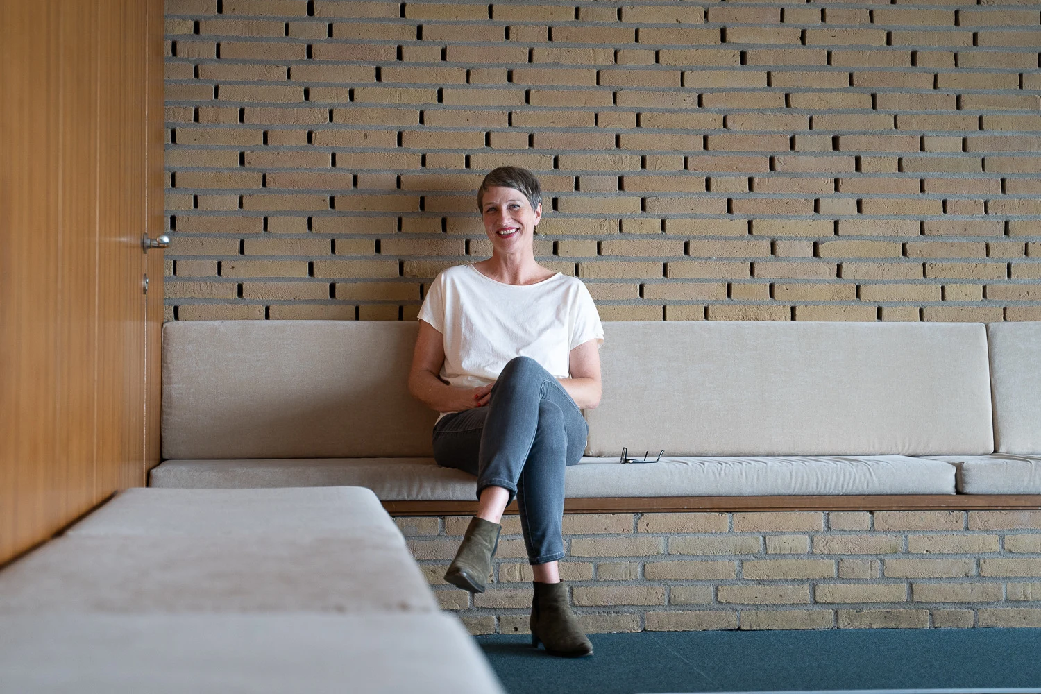 Katja Koehler lächelnd auf einer Sitzbank vor einer Backsteinwand